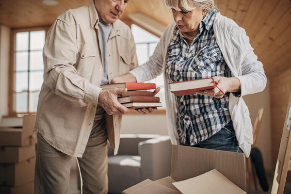 An older woman takes books from an older man struggling with Alzheimer’s rummaging.